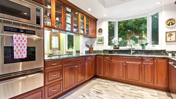 Una cocina moderna con armarios de madera, electrodomésticos de acero inoxidable y un amplio ventanal con vistas a zonas verdes.