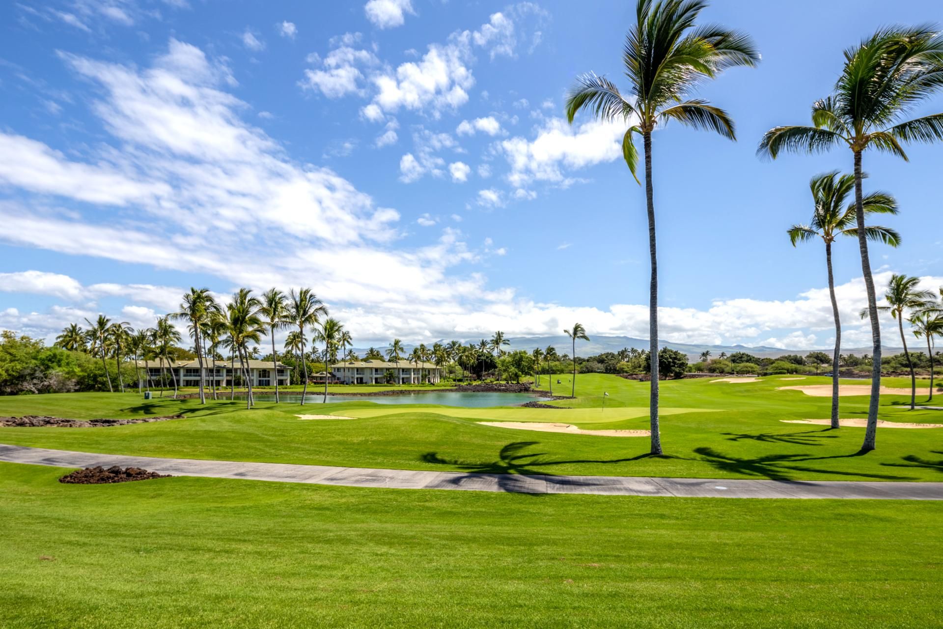 A golf course with a pond, palm trees, and a building in the background.