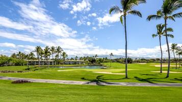 A golf course with a pond, palm trees, and a building in the background.