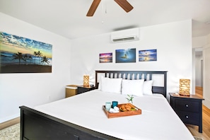 A bedroom with a bed, bedside tables, a ceiling fan, an air conditioner, and wall art.