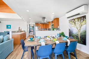 Une cuisine moderne avec des meubles en bois, un coin repas avec des chaises bleues et une grande fenêtre donnant sur une forêt.