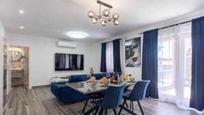 Een moderne woonkamer met een glazen eettafel, een blauwe bank en een aan de muur bevestigde televisie.