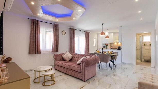 A modern living room with a pink sofa, a dining table, and a kitchen in the background. - Awesome home in Kastel Stari (Kastel Stari)