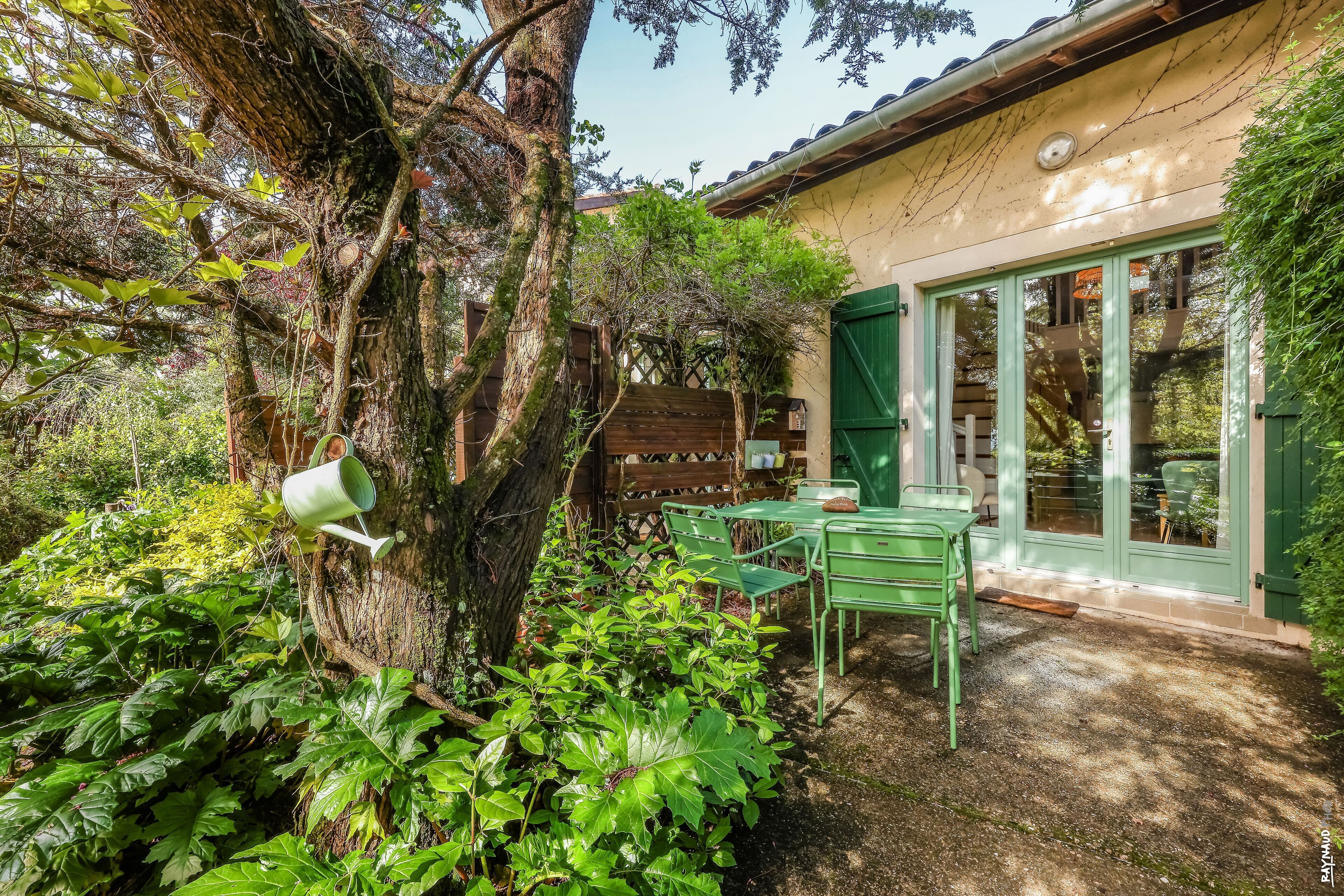 Un jardín con un banco de madera, una mesa y una puerta verde.