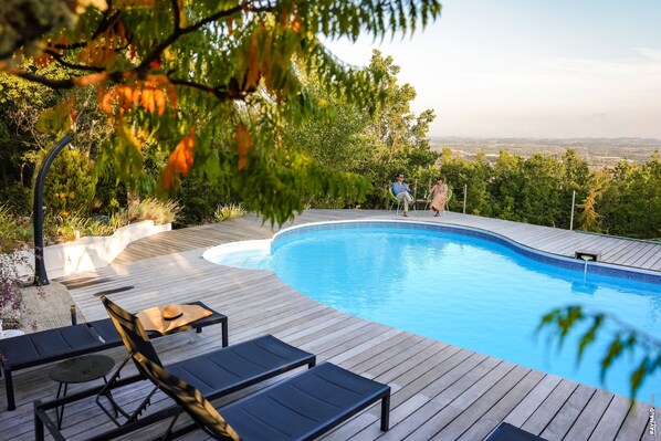 Une terrasse en bois avec une piscine, des chaises longues et une vue sur la ville.