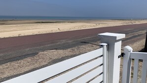 Une vue sur la plage avec un chemin pavé menant à l’eau, une clôture blanche et un ciel dégagé.