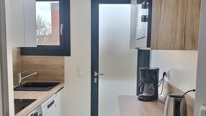 Une cuisine compacte avec des meubles blancs, un plan de travail en bois, un four encastré et une machine à café.
