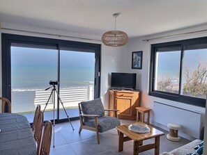 Un balcón con vista al mar, un telescopio, un televisor y asientos.