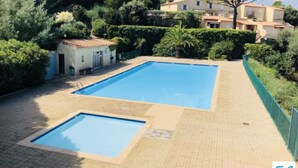 Una piscina rectangular con solárium empavedado, rodeada de vegetación y un edificio al fondo.