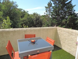 Un patio al aire libre con una mesa y sillas, rodeado por un muro de piedra bajo y follaje.