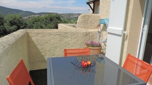 Una mesa con cubierta de vidrio, un frutero de metal, sillas naranjas y una maceta con flores.