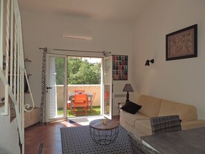 Un salon comprenant un canapé, une table basse, une lampe et une porte-fenêtre coulissante donnant sur une terrasse extérieure avec une table et des chaises.