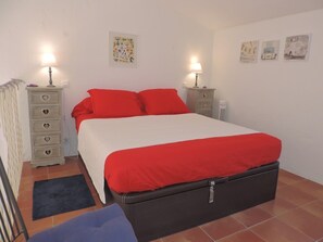 Un dormitorio con una cama, dos mesitas de noche, un aparador y decoración en la pared.