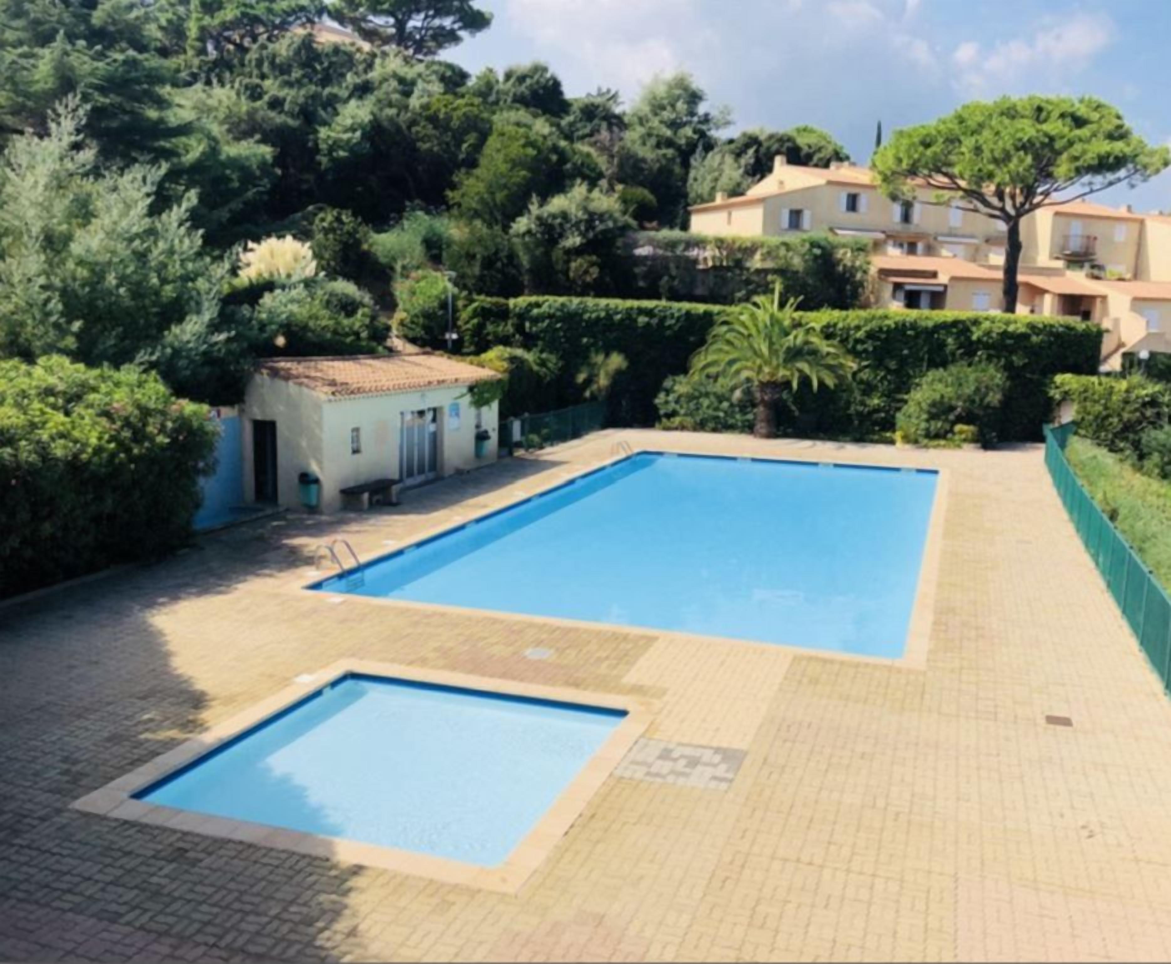Ein rechteckiger Pool mit einer gefliesten Terrasse, umgeben von Grünflächen und einem Gebäude im Hintergrund.