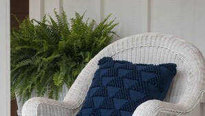 Una silla de mimbre blanca con un cojín azul oscuro y una manta tejida.