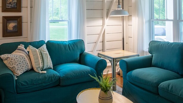 Una habitación acogedora con un sofá color turquesa, una mesita redonda con una planta y una escalera con vigas blancas.