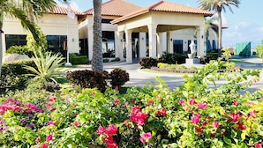 Ein Hotel mit rotem Ziegeldach, Palmen und einem gepflegten Garten mit rosa Blumen.