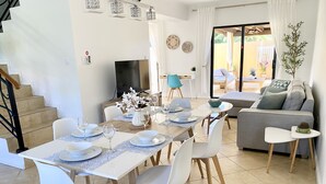 Ein moderner Essbereich mit einem langen Tisch, gedeckt für vier Personen, weißen Stühlen und einer Vase mit Blumen.