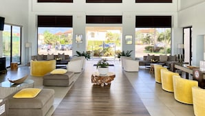 Eine großzügige Lobby mit einem zentralen Couchtisch, Sofas und Sesseln, die darum angeordnet sind. Große Fenster bieten Ausblicke nach draußen.