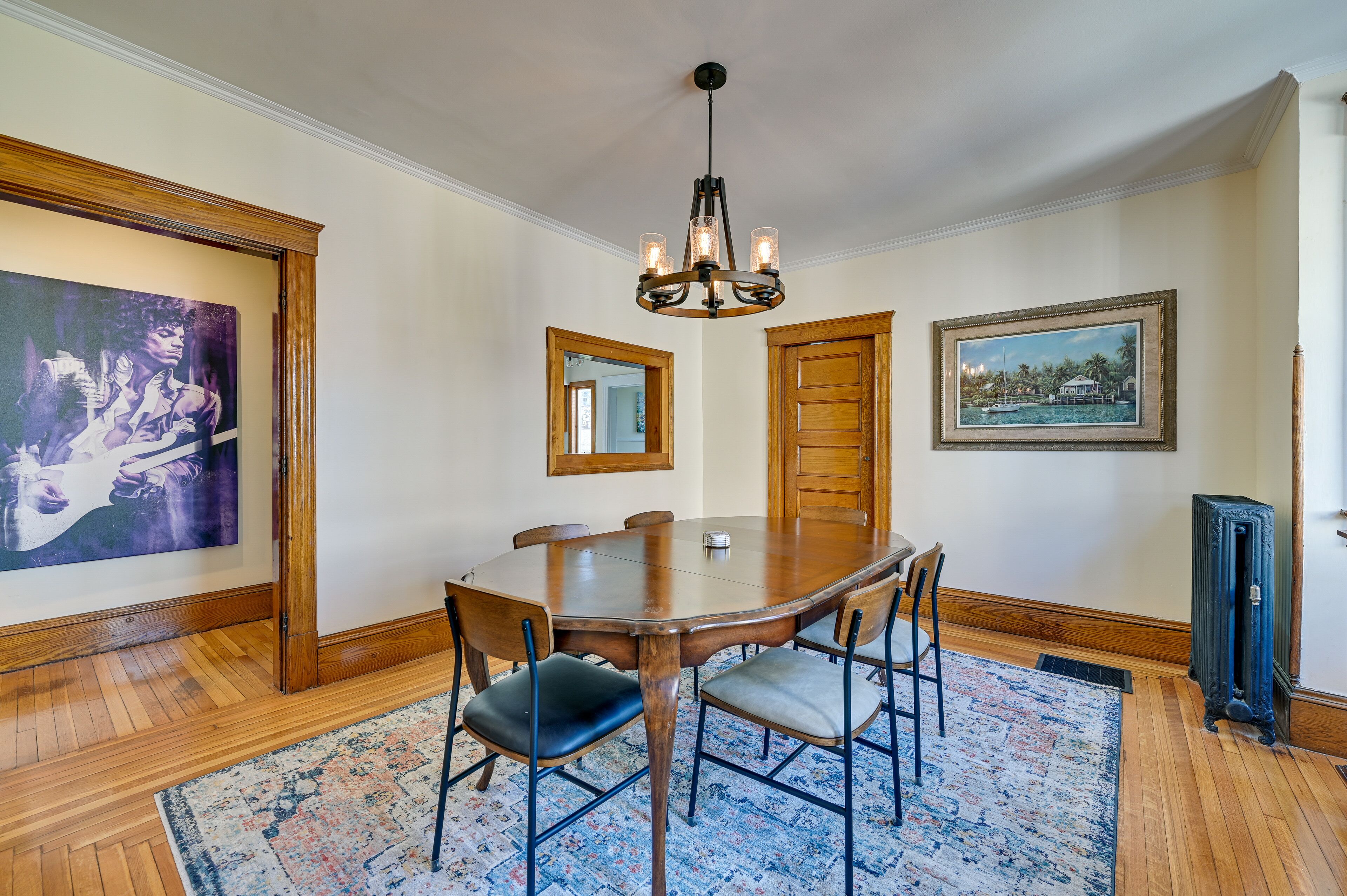A dining room with a wooden table, chairs, a chandelier, and artwork on the walls.
