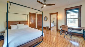 A four-poster bed with a wooden headboard, a desk with a chair, and a large window with blinds. - Spacious Historic Home in the Berkshires! (Pittsfield)