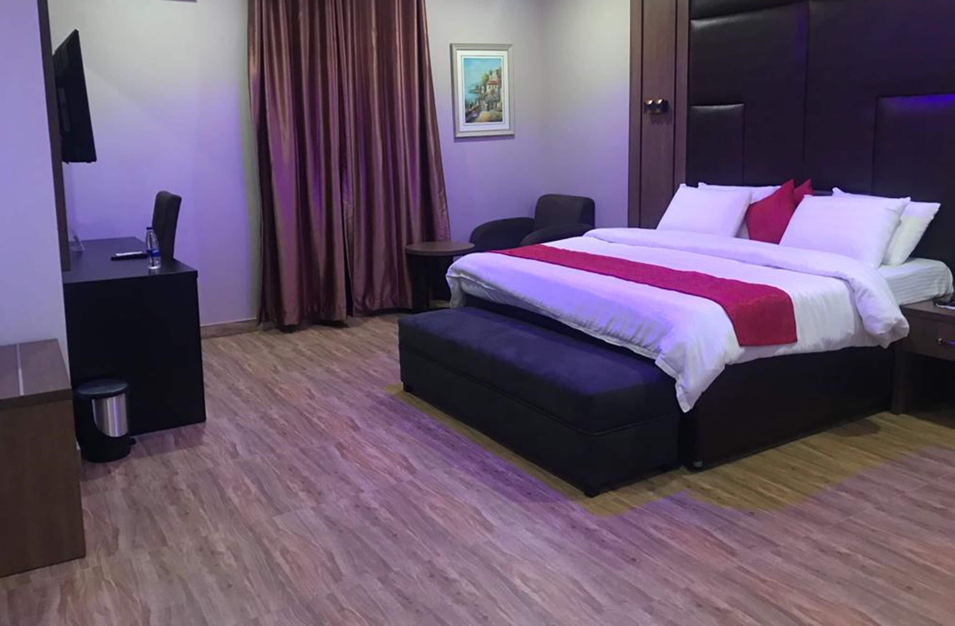 Una habitació d'hotel amb un llit, escriptori, cadira, televisió i un quadre a la paret.
