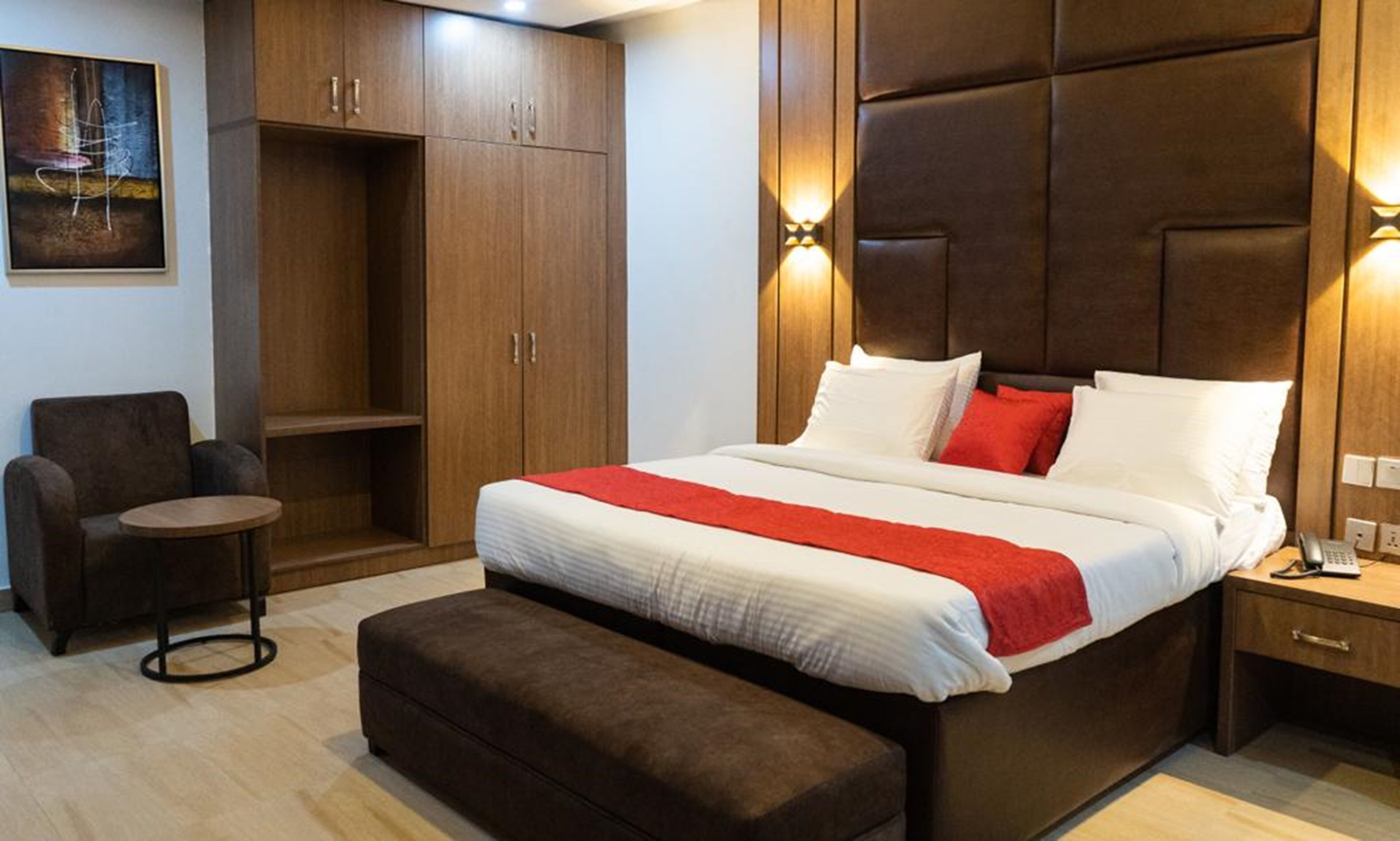 A modern hotel room with a large bed, a small seating area, and a wardrobe.
