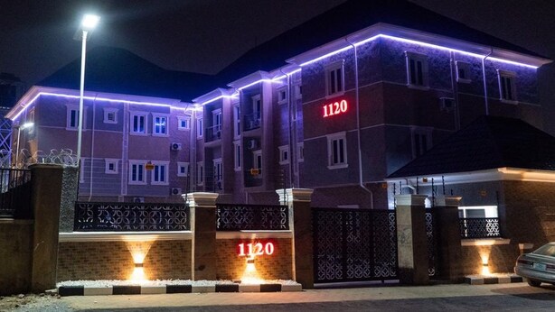 A multi-story building with a prominent address sign '1120' at the entrance, illuminated by ground lights.