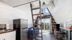 A kitchen with a stainless steel refrigerator, a wooden ladder, a blue sofa, and a bar stool. - Tiny AFrame/Fire Pit/Pets/Lake Access/Dogwood Canyon (Lampe)