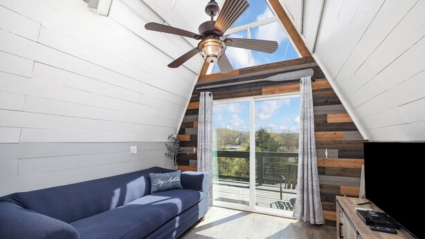 A modern living room with a blue sofa, a ceiling fan, and a large sliding glass door leading to an outdoor area. - Tiny AFrame/Fire Pit/Pets/Lake Access/Dogwood Canyon (Lampe)