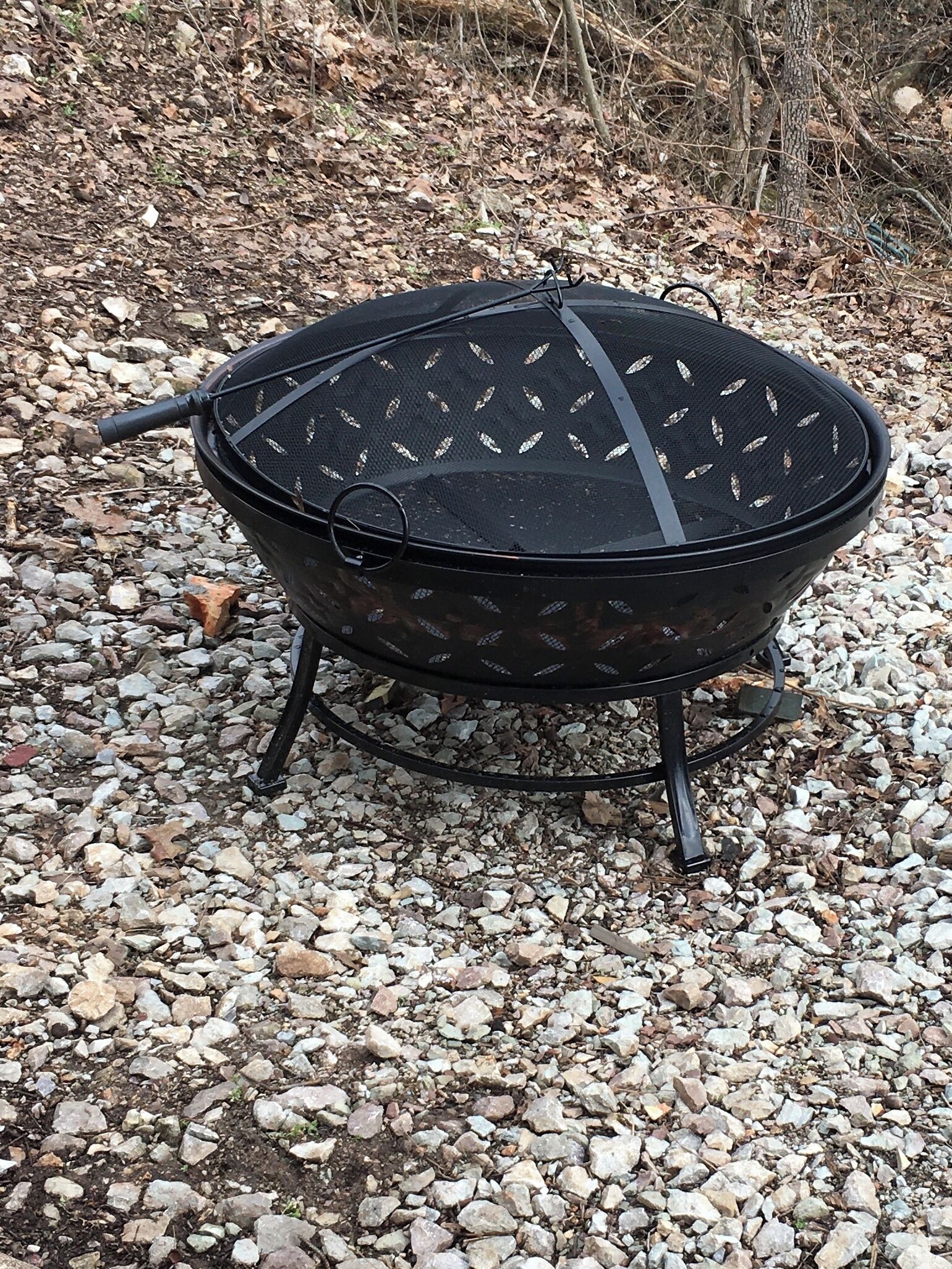 Ein tragbarer Grill mit Netzabdeckung und Tragegriff, auf Kies.