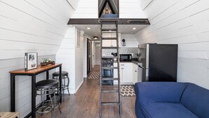 Une cuisine compacte avec un espace nuit en mezzanine, accessible par une échelle, et un coin repas avec des tabourets.