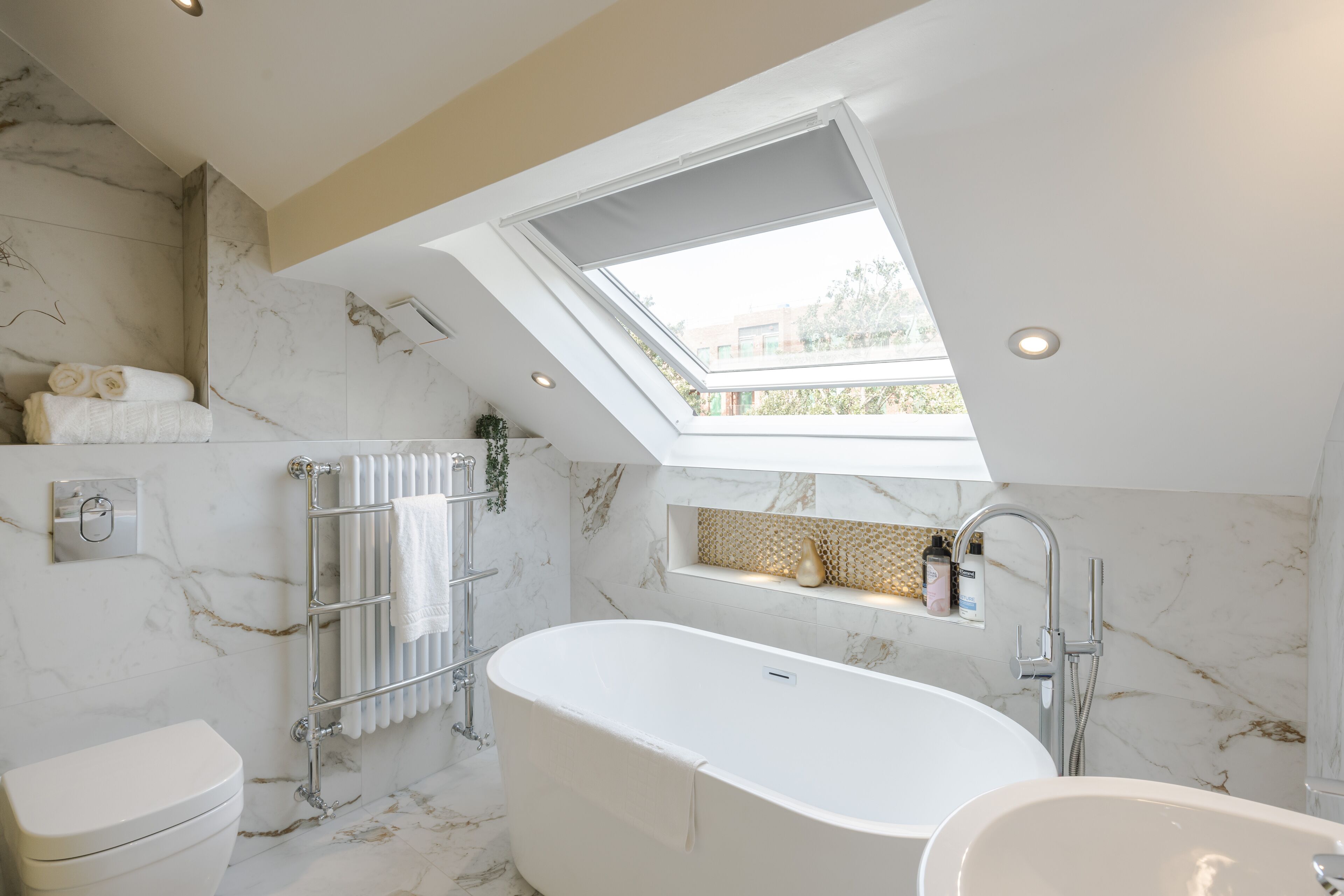 A modern bathroom with a skylight, a freestanding bathtub, a toilet, and a towel rack.