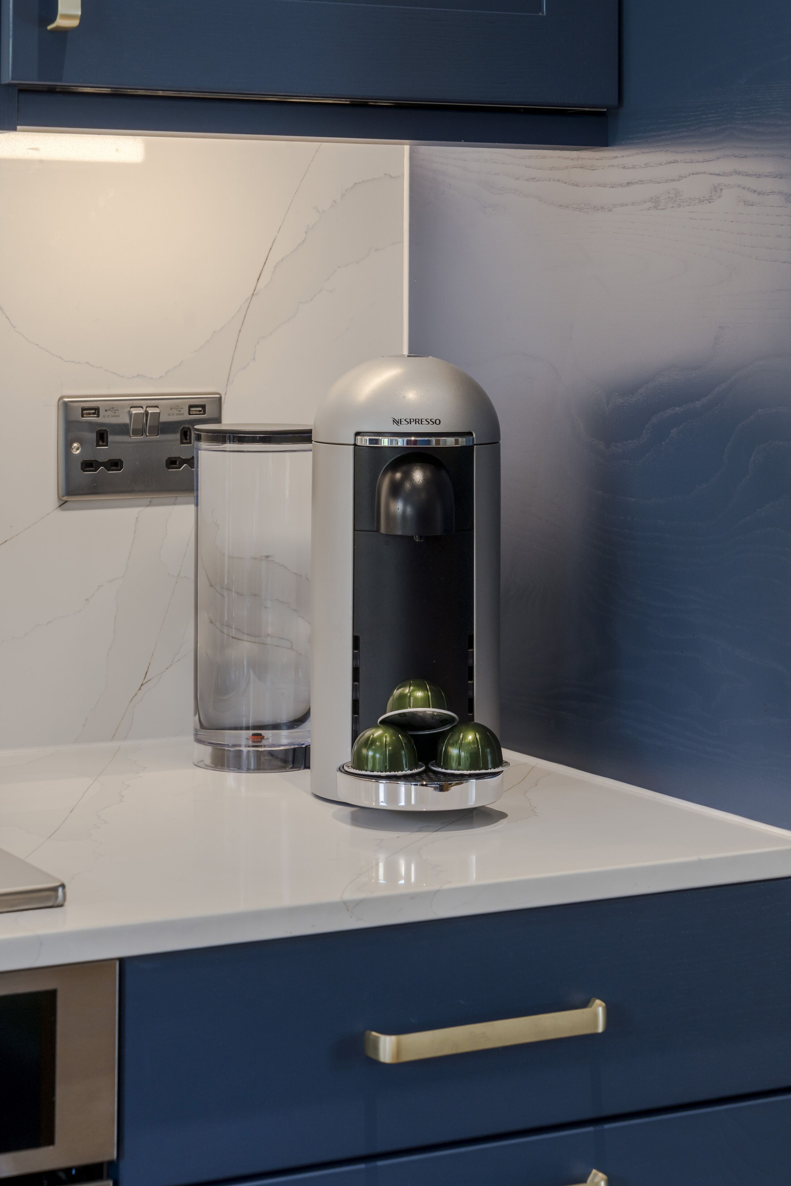 A kitchen with a Nespresso coffee machine, a glass container, and a blue cabinet.