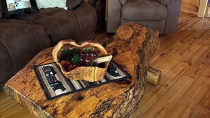 Ein gemütliches Wohnzimmer mit einer braunen Ledersofa, einem Holztisch mit einer Obstschale und einem Holzstuhl. Im Hintergrund ist eine Treppe mit einem Holnänder zu sehen.
