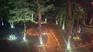 Ein Außenbereich bei Nacht mit Bäumen und einem von Lichterketten beleuchteten Weg.