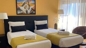 A hotel room with two beds, a painting on the wall, and a window with curtains.