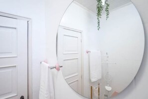 A bathroom with a large round mirror, a white door, and a hanging plant.