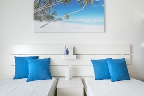 A bedroom with two beds, a white headboard, and a framed picture of a beach scene.