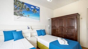 Habitación de hotel con dos camas, cada una con ropa de cama azul y cabeceros blancos. Se observa un armario grande de madera y un cuadro de una playa tropical en la pared.