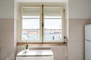 Ein Badezimmer mit Fenster, einem weißen Waschbecken und einer Topf-Orchidee.