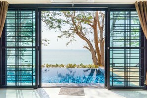 Blick durch eine Schiebetür auf einen Pool mit freiem Blick auf das Meer und einen Baum.