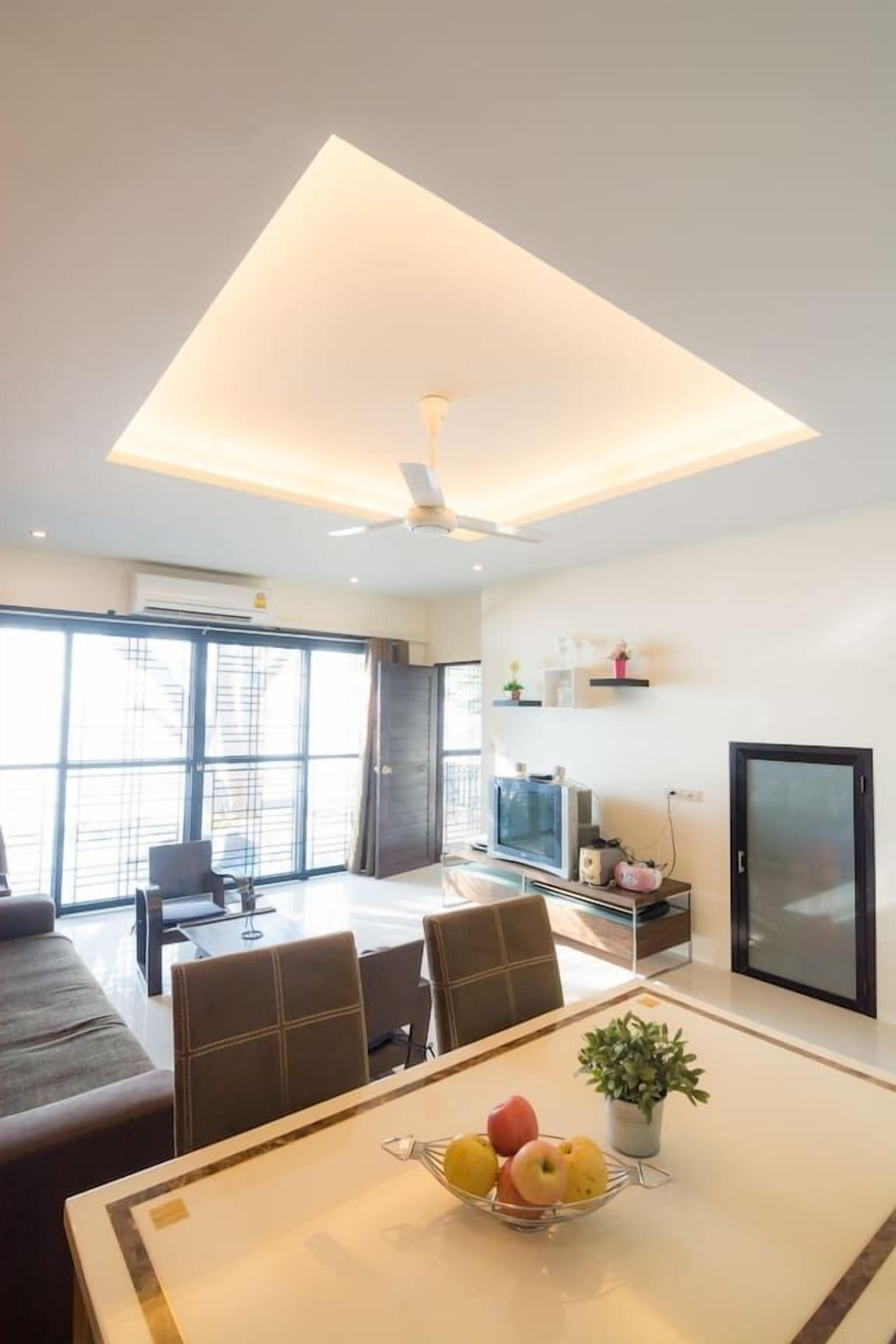 A modern living room with a dining area, large windows, and a ceiling fan.