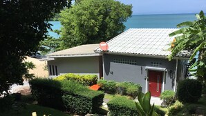 Una casa con puerta roja, rodeada de follaje cuidado y vistas al mar.