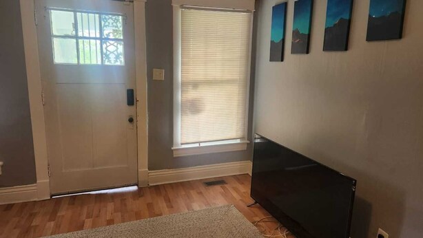 A room with a door, a window with blinds, a flat-screen TV, and wall-mounted artwork. - Derby rental furnished 2BR, 1 full bath(shower/tub) house (Louisville)