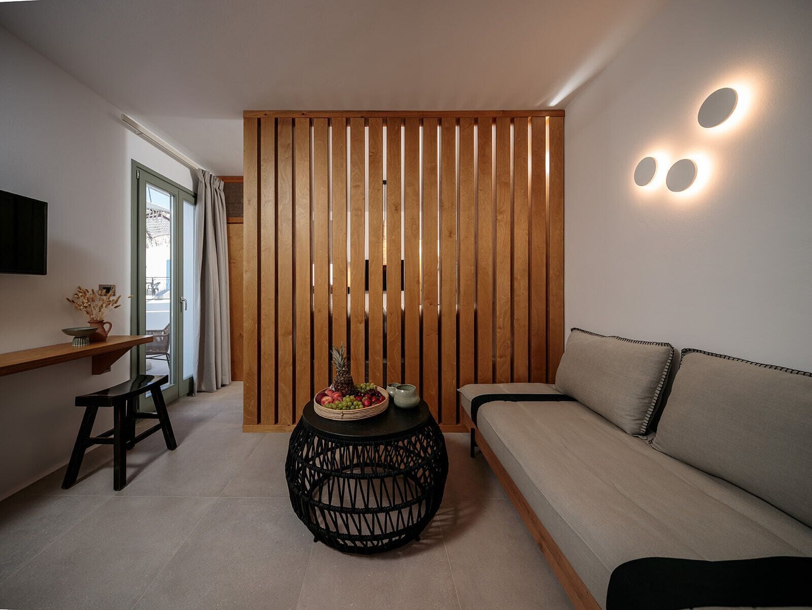 A modern living room with a sofa, a round black woven table, and a wooden partition.