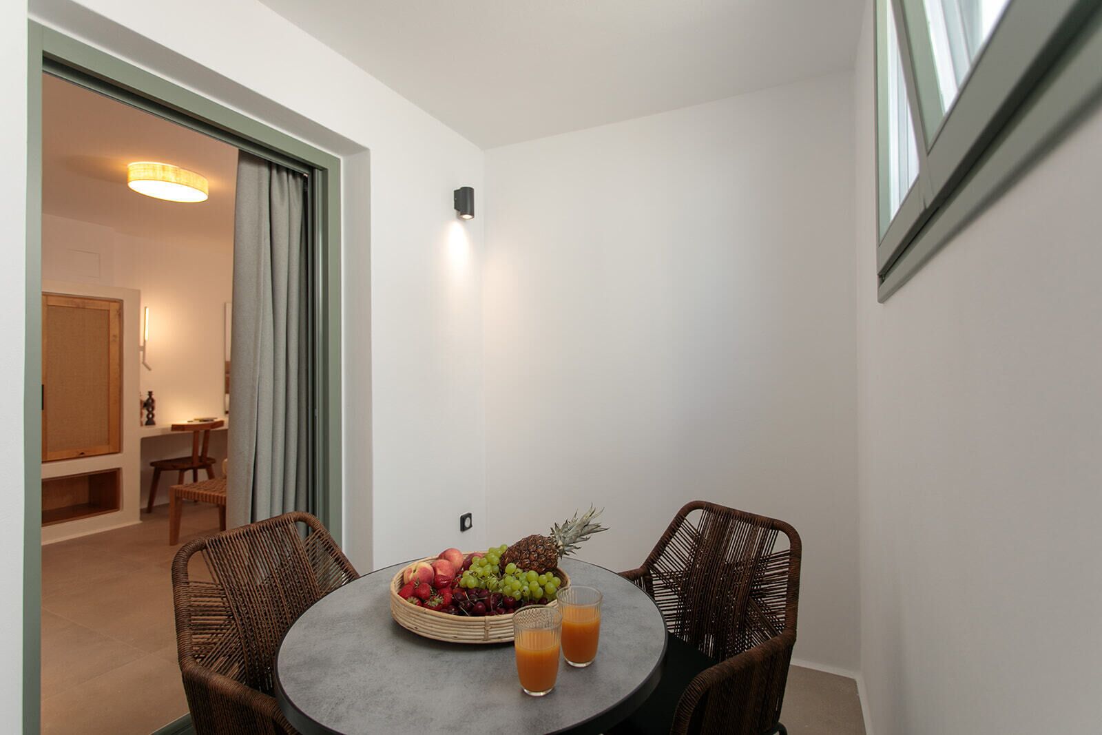 A small dining area with a round table, wicker chairs, a fruit bowl, and two glasses of orange juice.