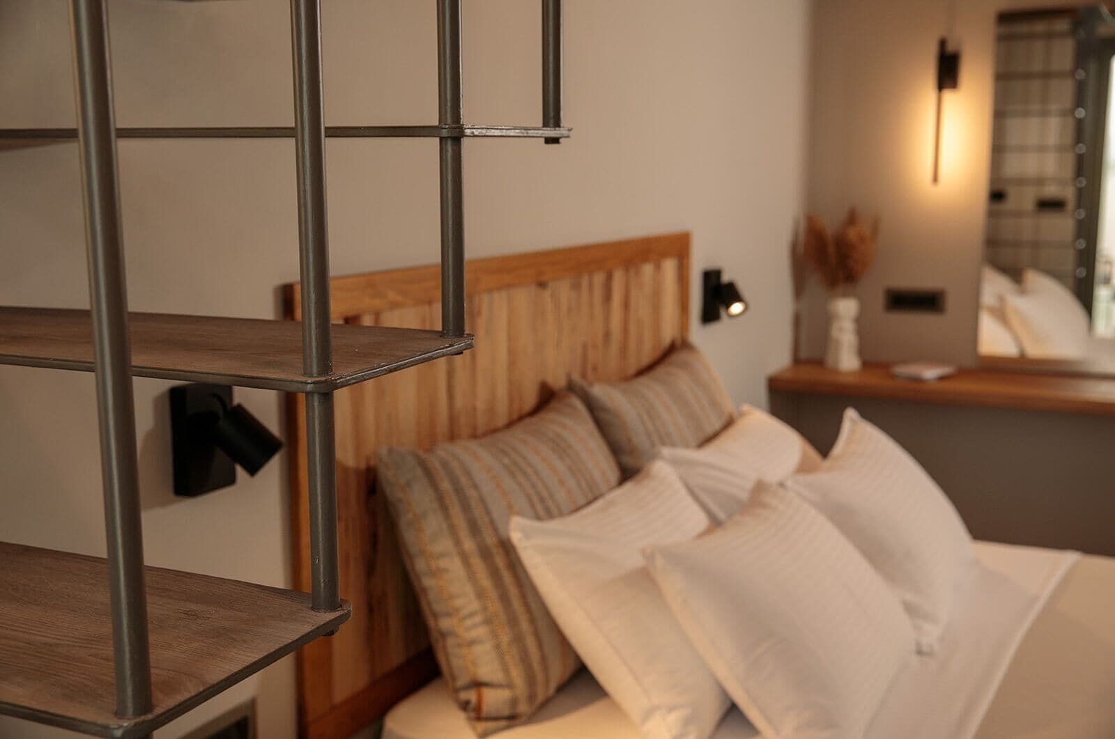 Ein Hotelzimmer mit Holz-Kopfteil, mehreren Kissen, einem Metallregal und einer Wandleuchte.
