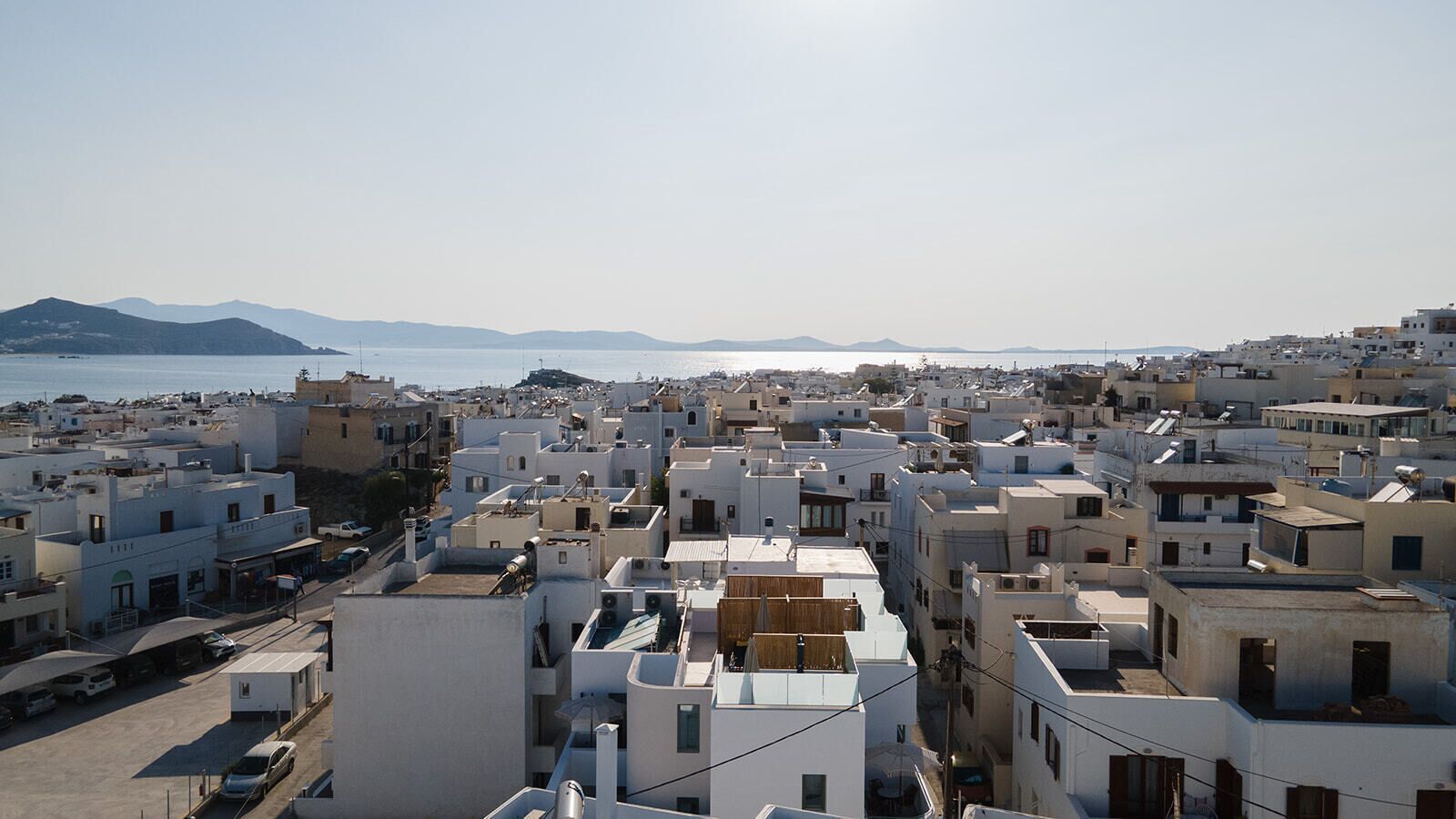 Un pueblo costero con edificios blancos, cielo despejado y vistas al mar y montañas lejanas.