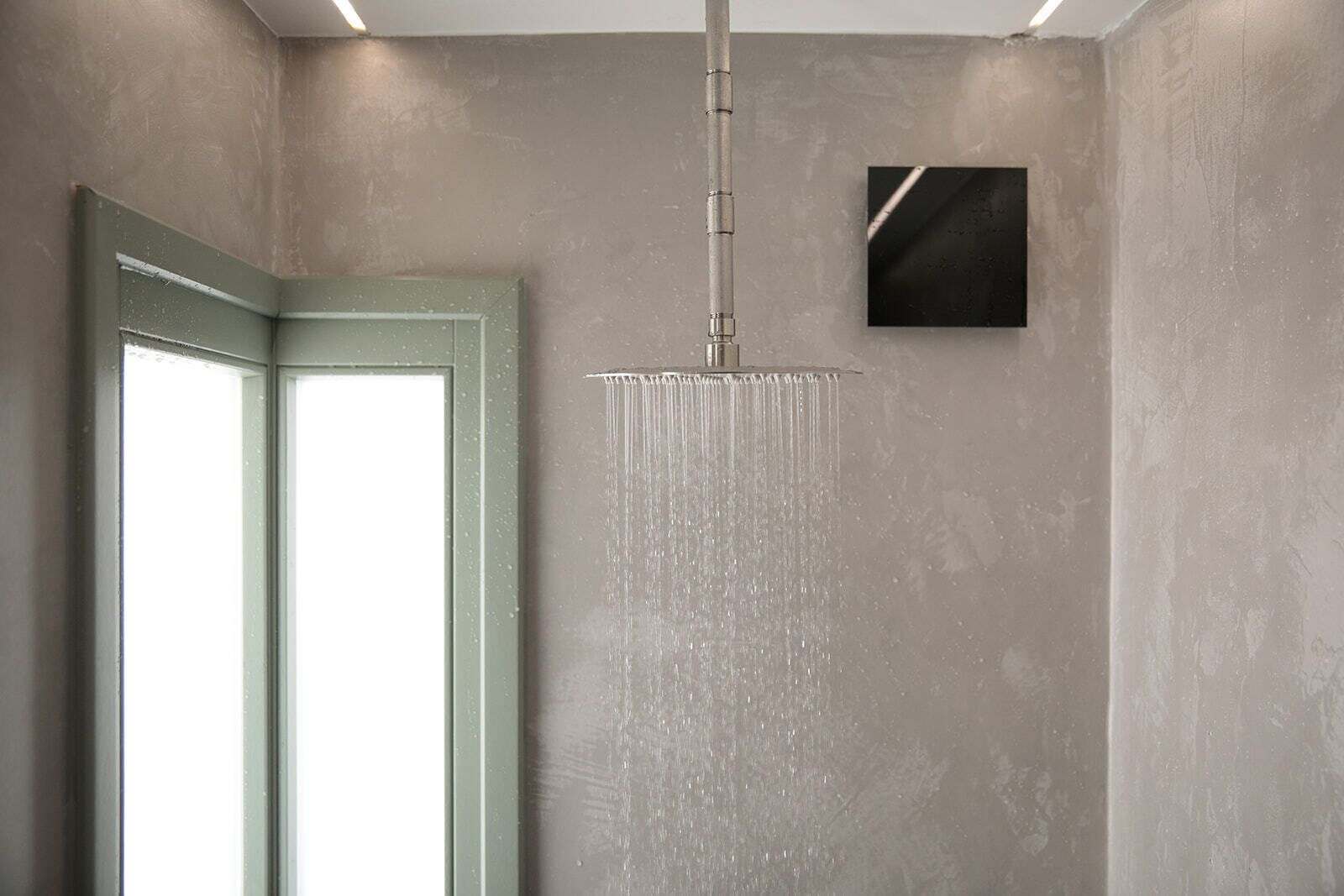 Une douche dotée d’un pommeau de douche à pluie vertical, une porte avec des panneaux en verre dépoli et un mur à texture.